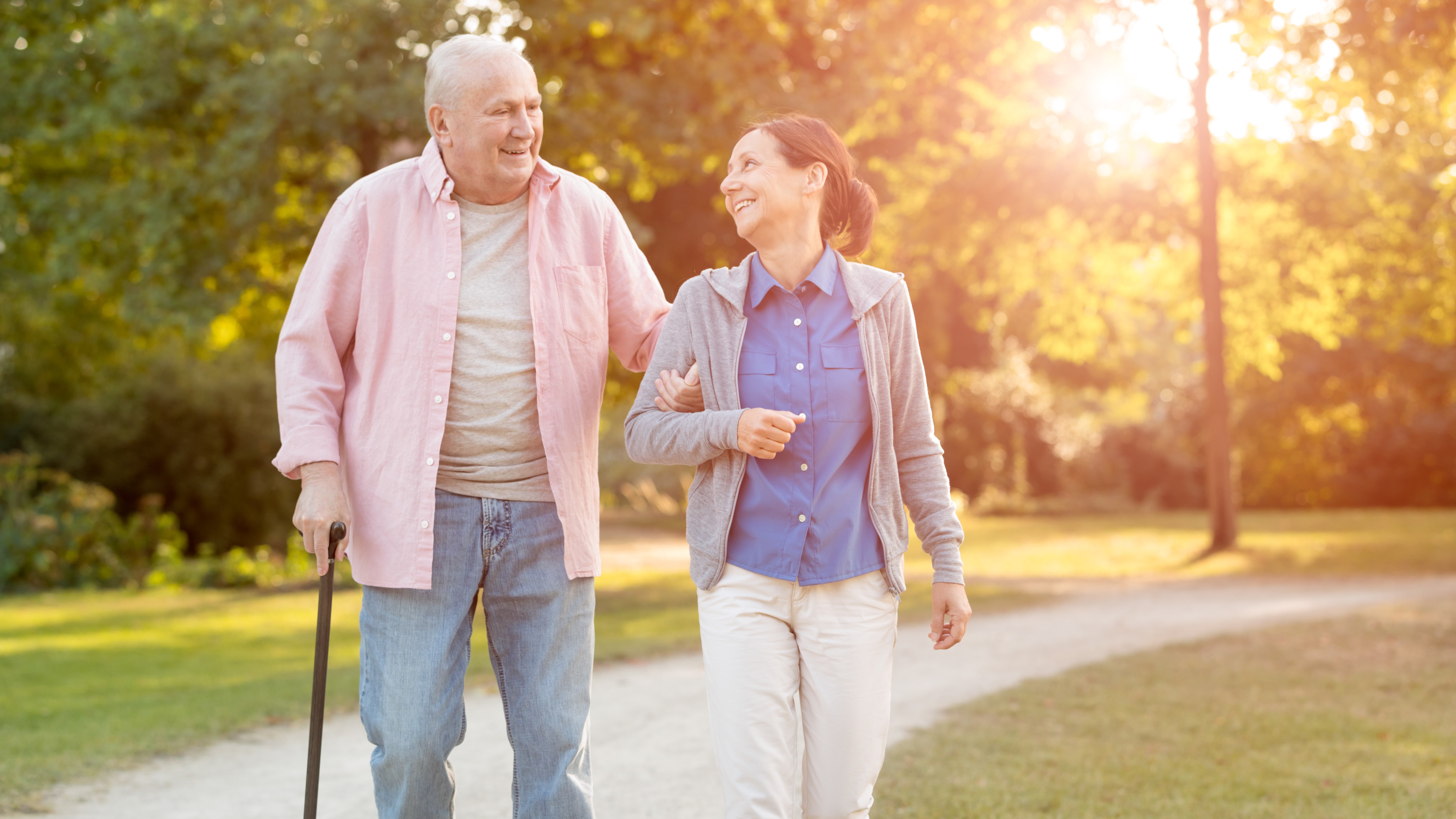 Female caregiver and older man with cane walking in a park