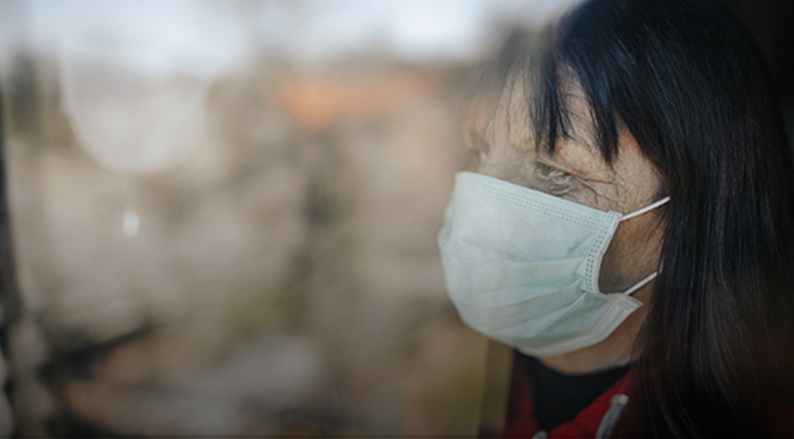 Senior woman wearing a mask looking through nursing home window